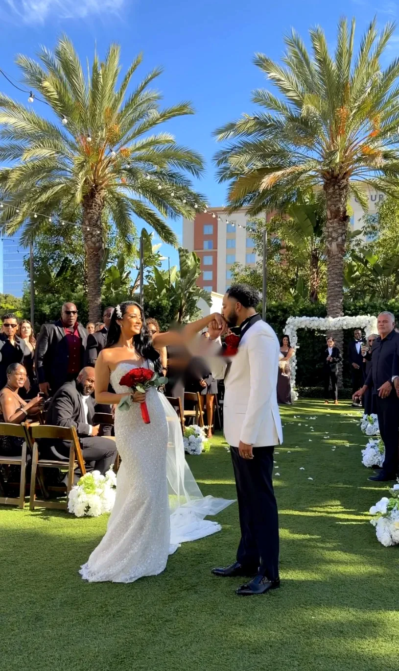 Groom kisses the bride's hand at a garden ceremony under palm trees