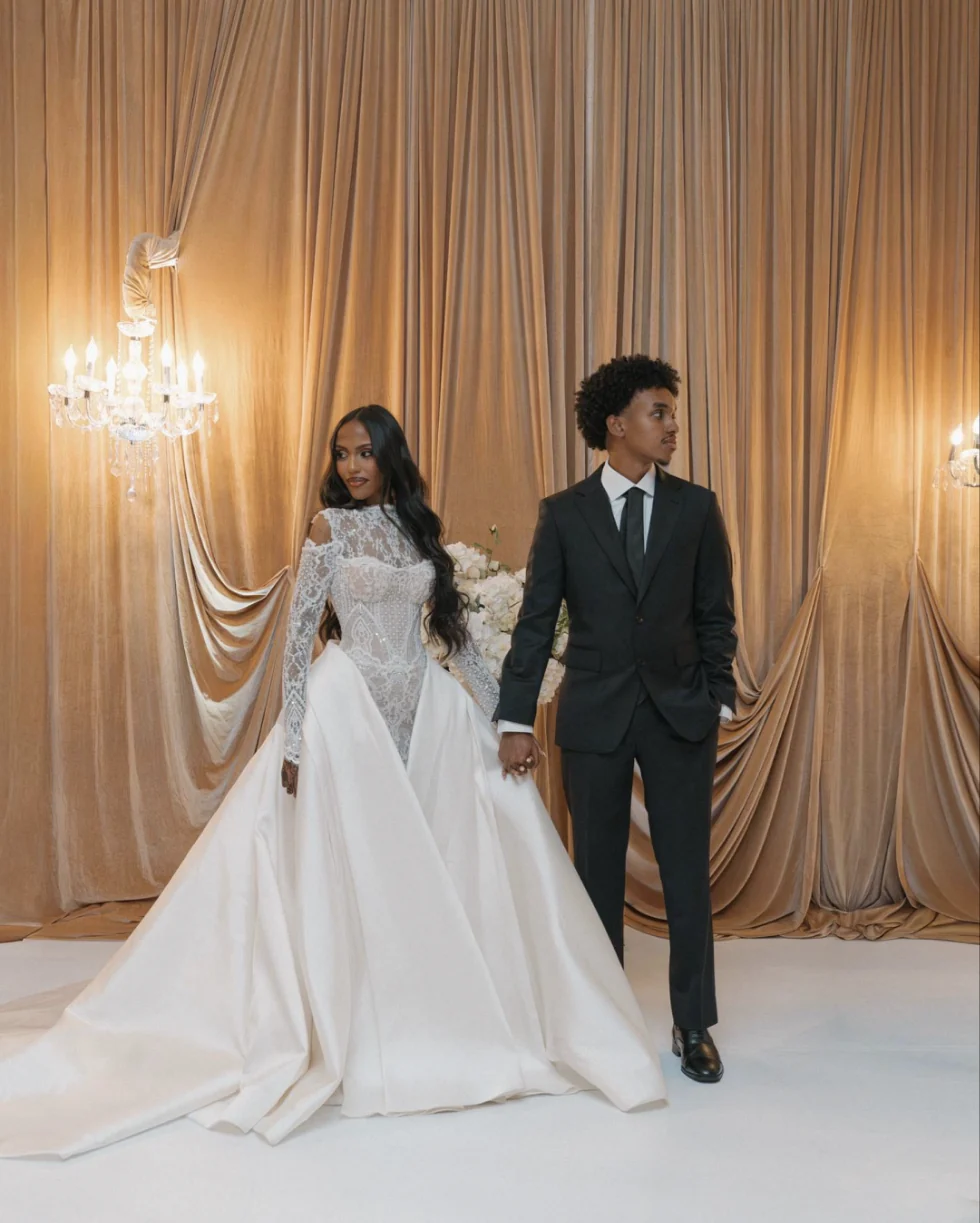 Bride and groom holding hands in front of champagne velvet draping and crystal chandeliers